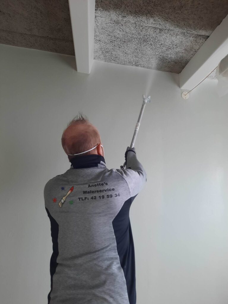 Maler sprøjter maling på loft i rum