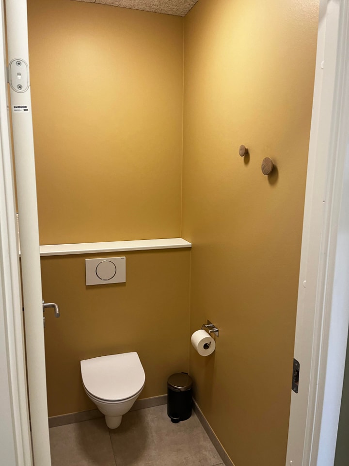 Lille badeværelse med væghængt toilet og gule vægge